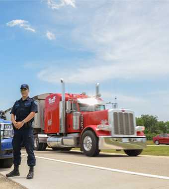 Motor Carrier Officer standing beside cruiser with truck in background